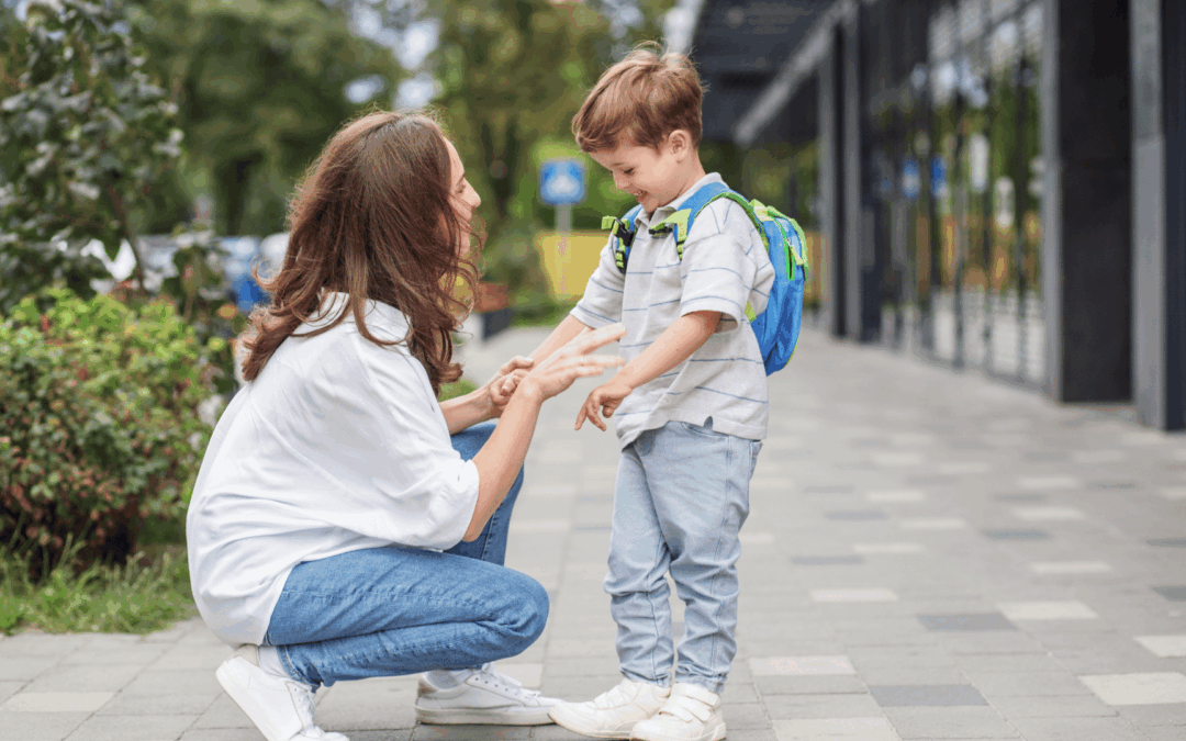 Mother kneeling to greet a smiling boy with a blue backpack on a city sidewalk, preparing for a high-five or touch.