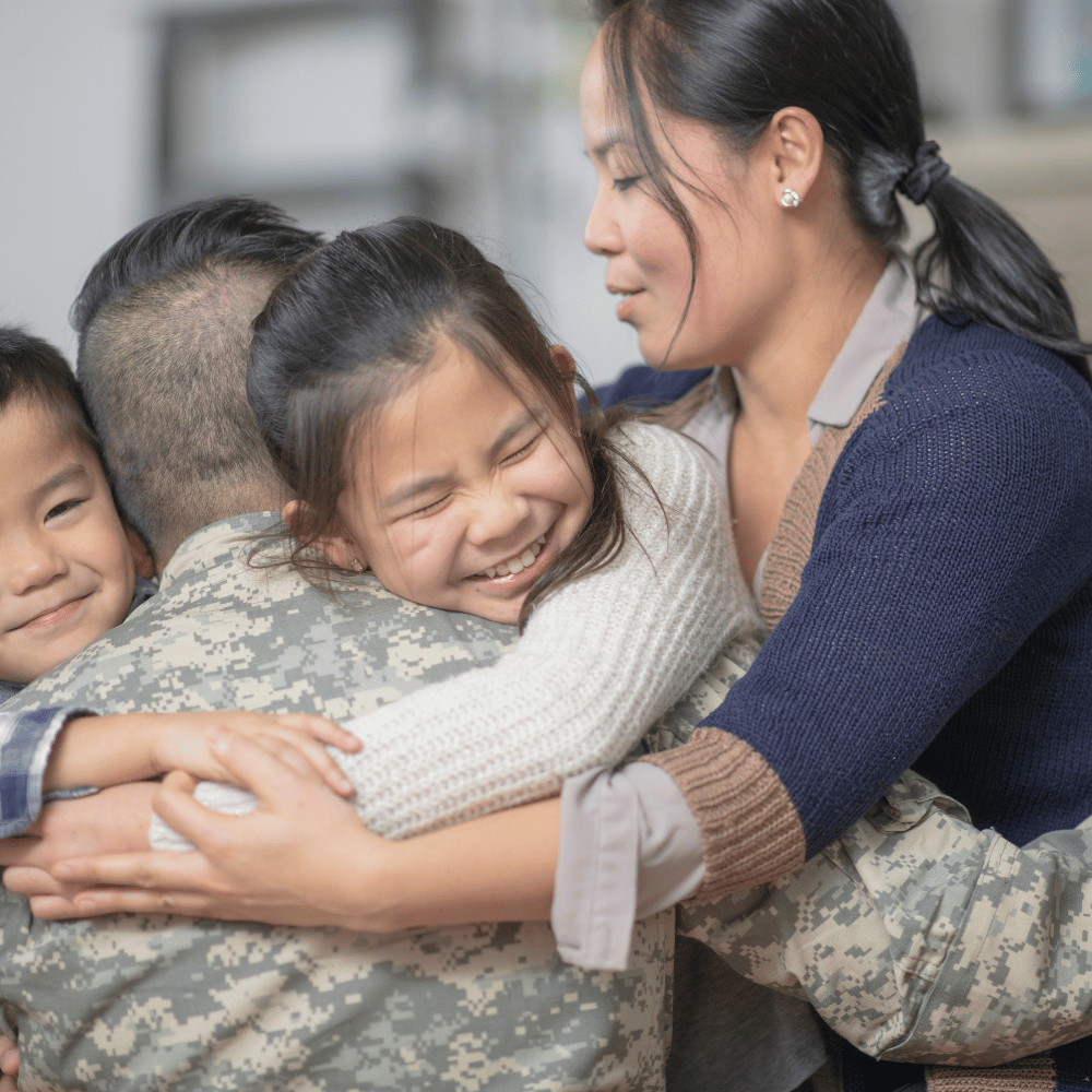 Family in a warm hug: a soldier in camouflage embraces a smiling woman and two children at a reunion.